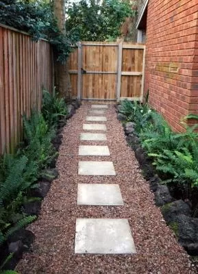 A side yard garden path with large square paver stones surrounded by red rubber mulch.