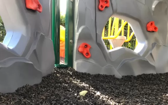 Playground climbing wall with brown rubber mulch flooring for added fall height safety.